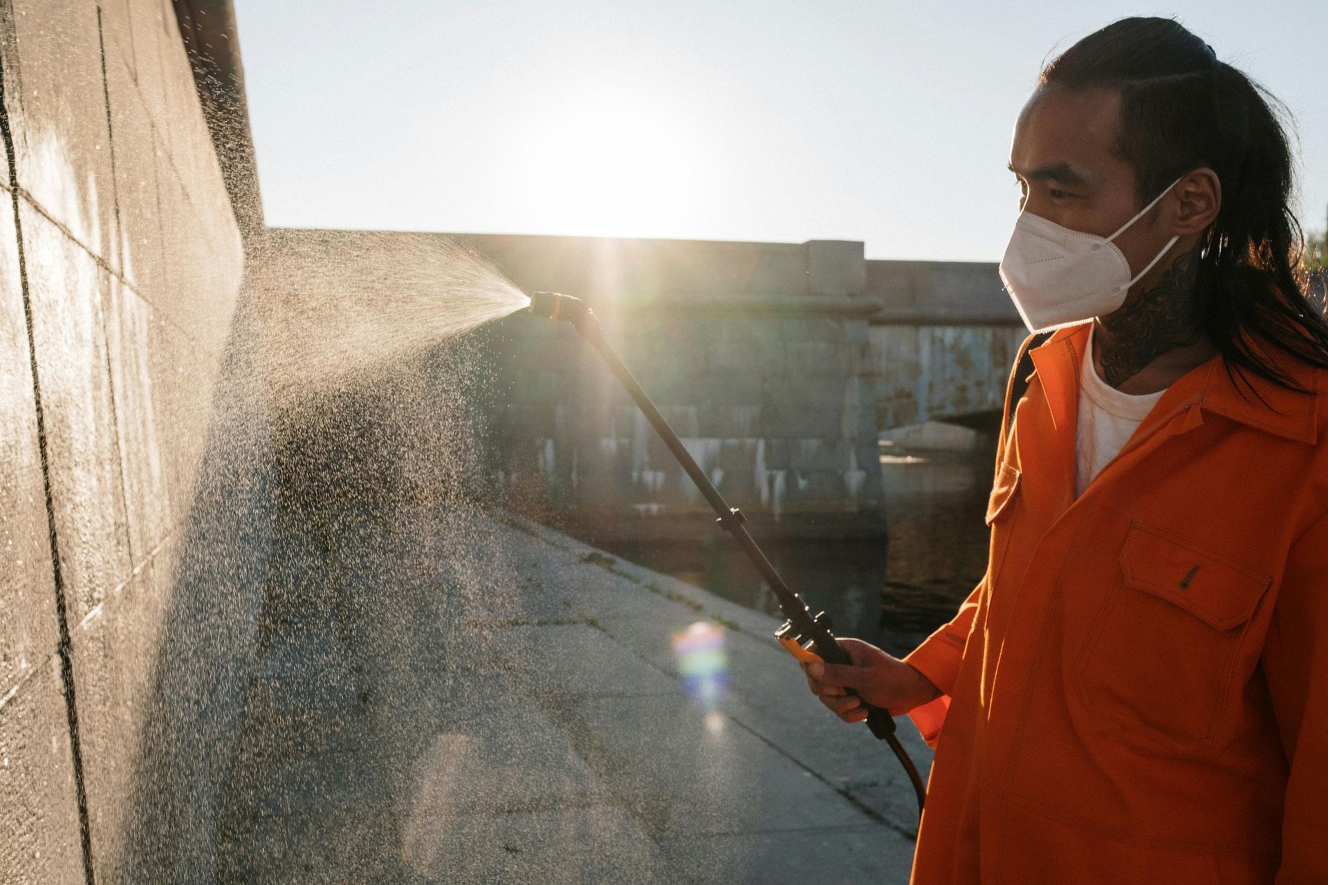 A man wearing a mask is spraying a wall with a hose.