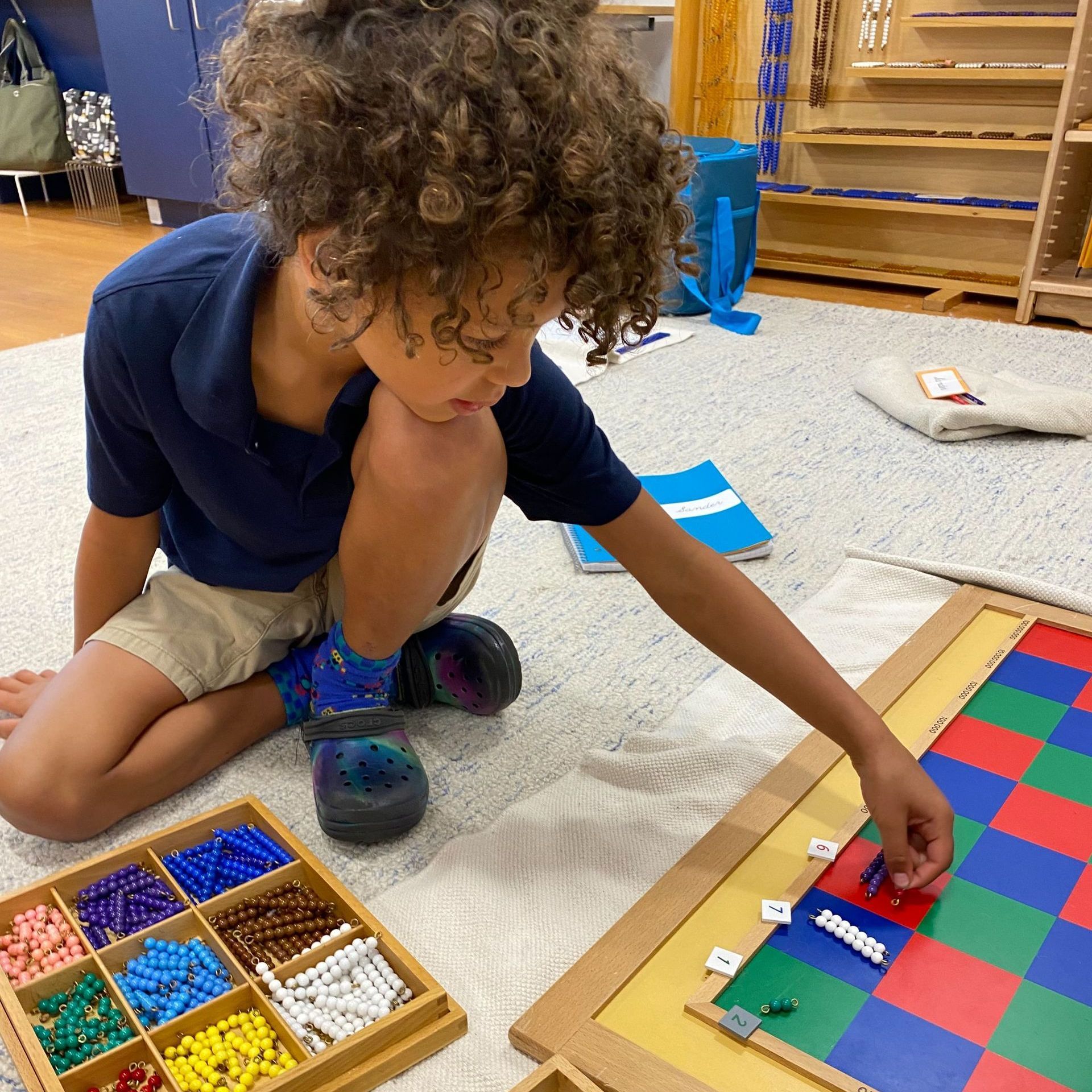 a Montessori child is sitting on the floor playing with beads