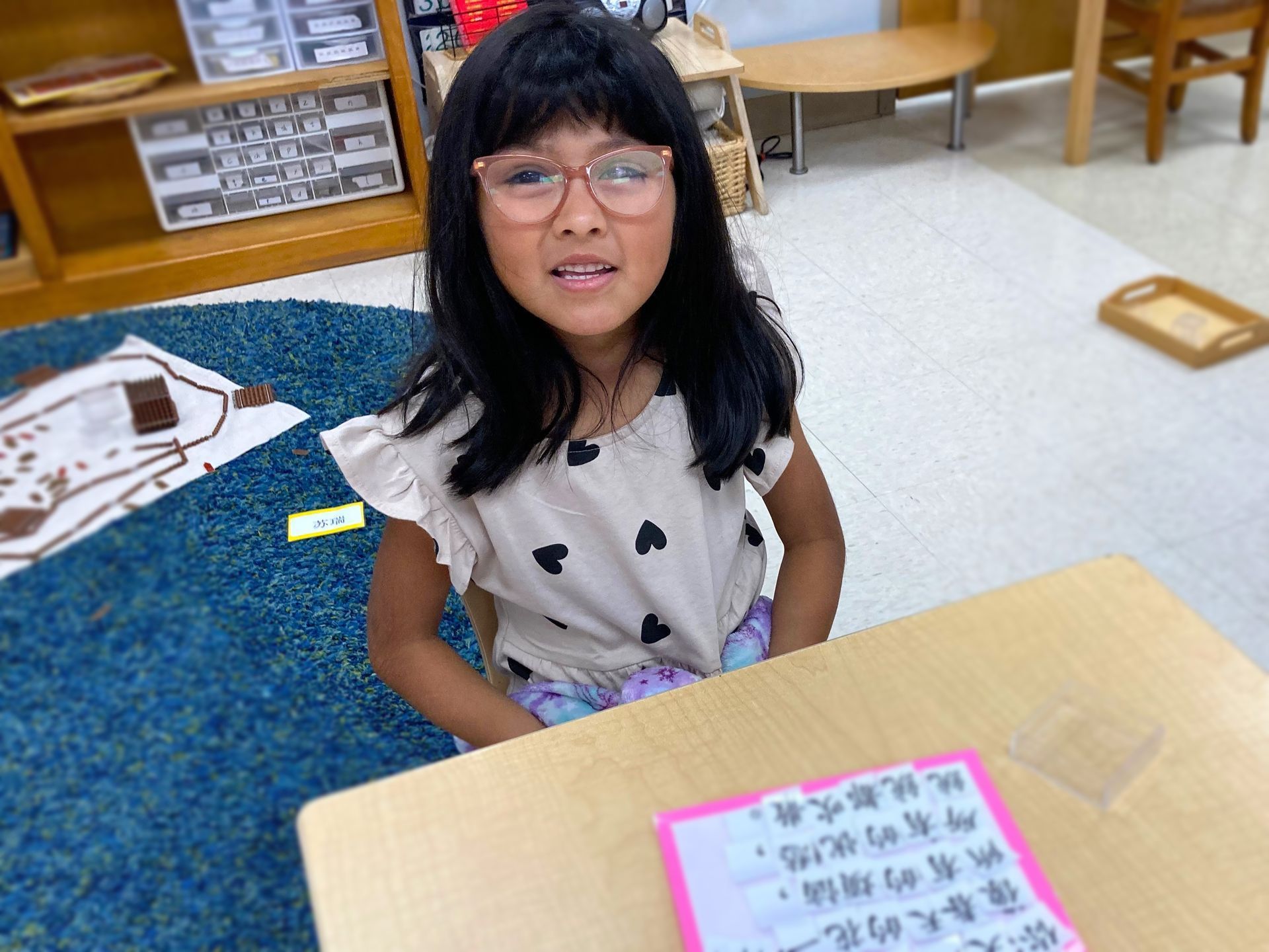 a Montessori child wearing glasses is sitting at a desk in a classroom