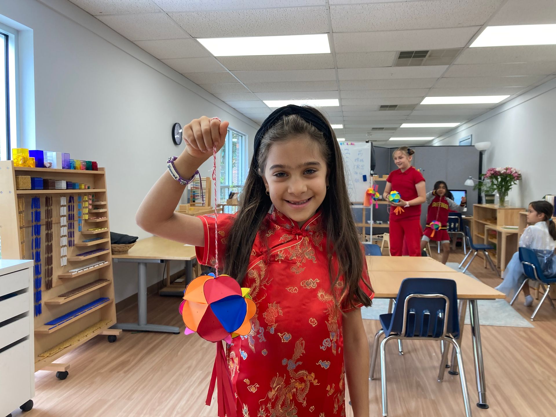 a Montessori child in a red dress is holding a ball in a classroom