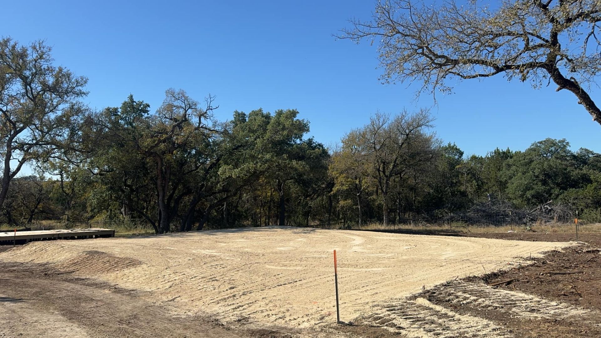 Gravel-covered lot, orange stake, trees in the background, blue sky.