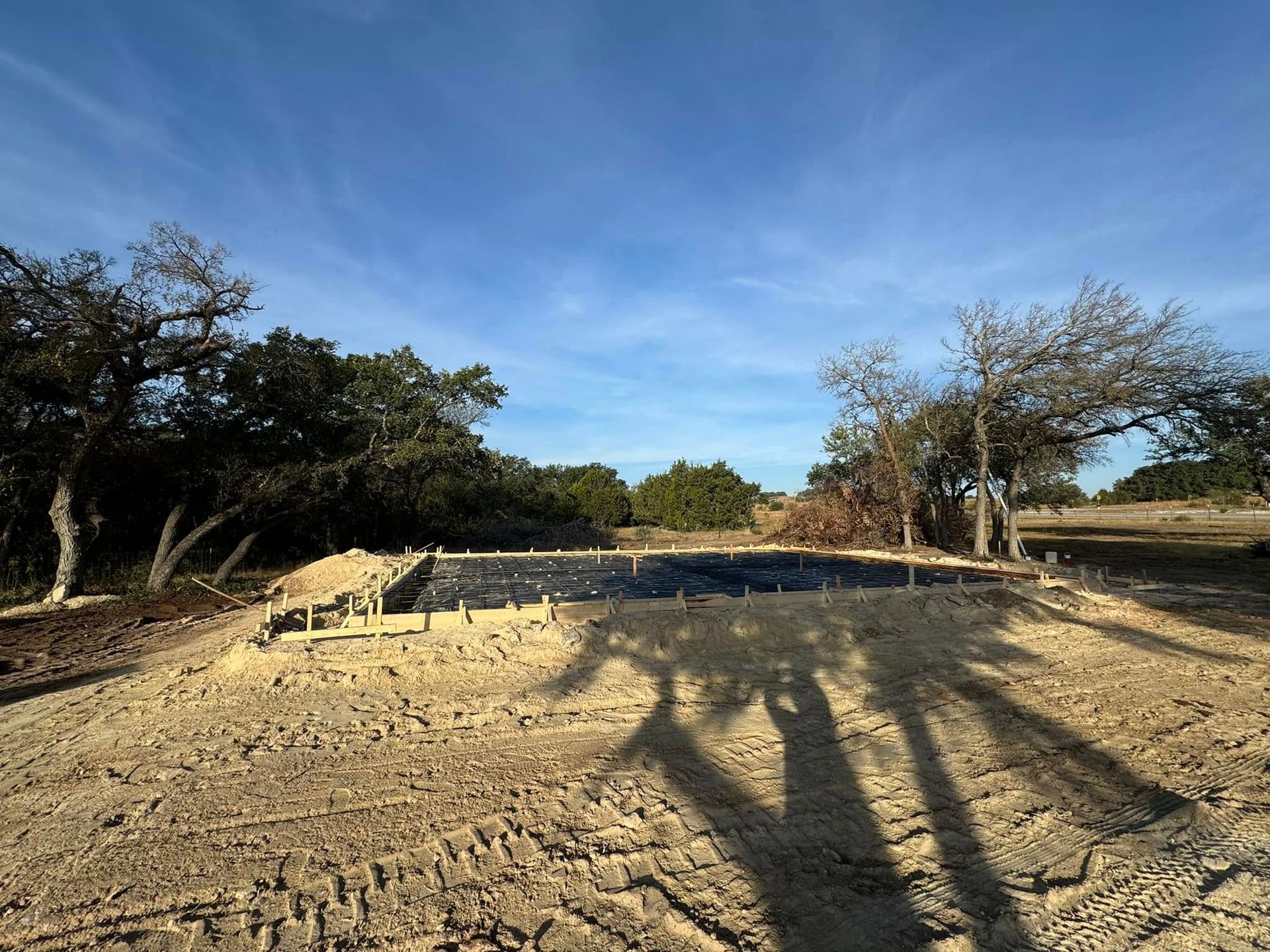 Construction site with wooden frame, covered in black material, in a sandy field under a blue sky.