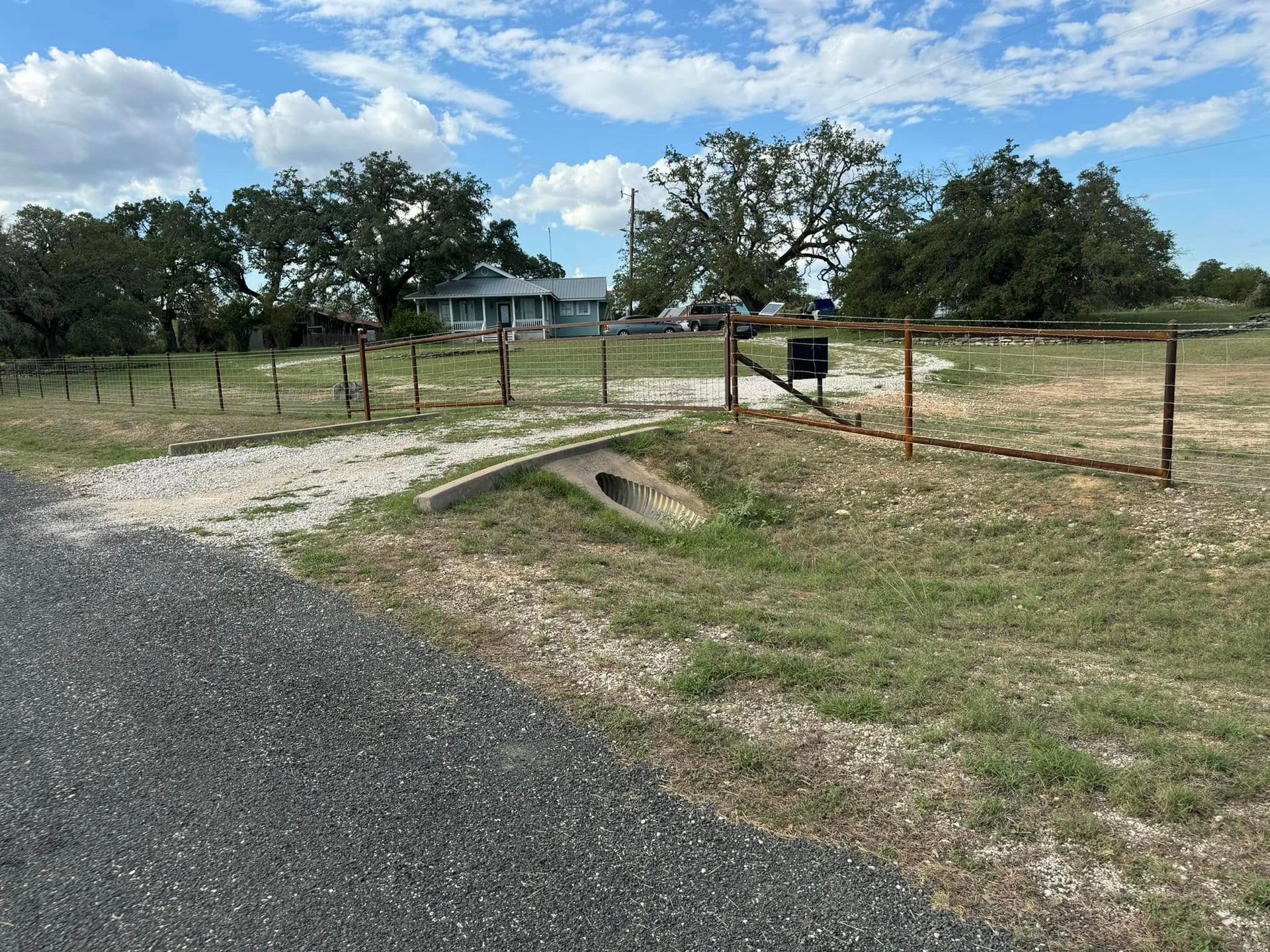 Gravel driveway leading to a rural property with a house, mailbox, and trees on a partly cloudy day.