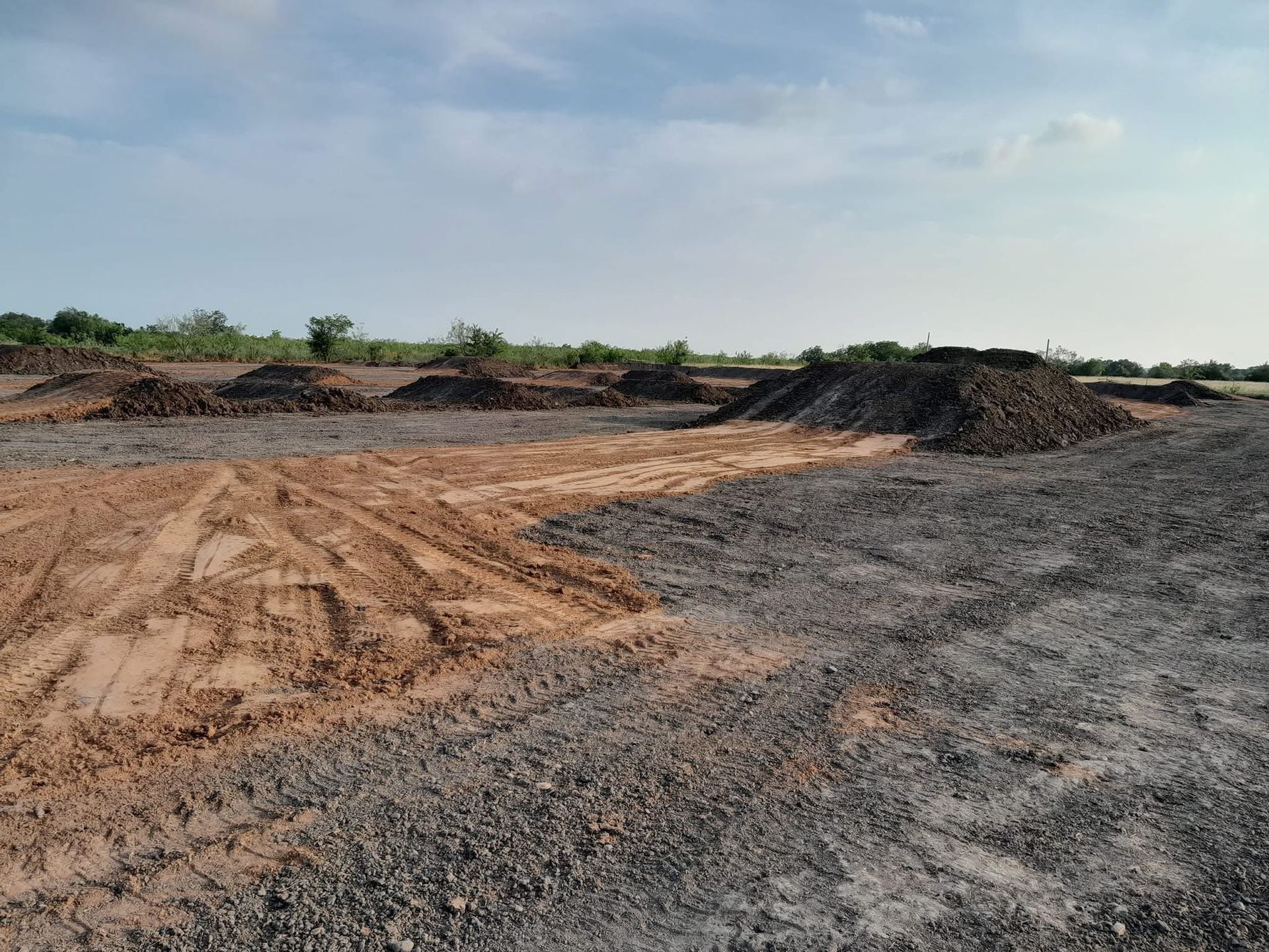 Open field with piles of dark earth under a cloudy sky.