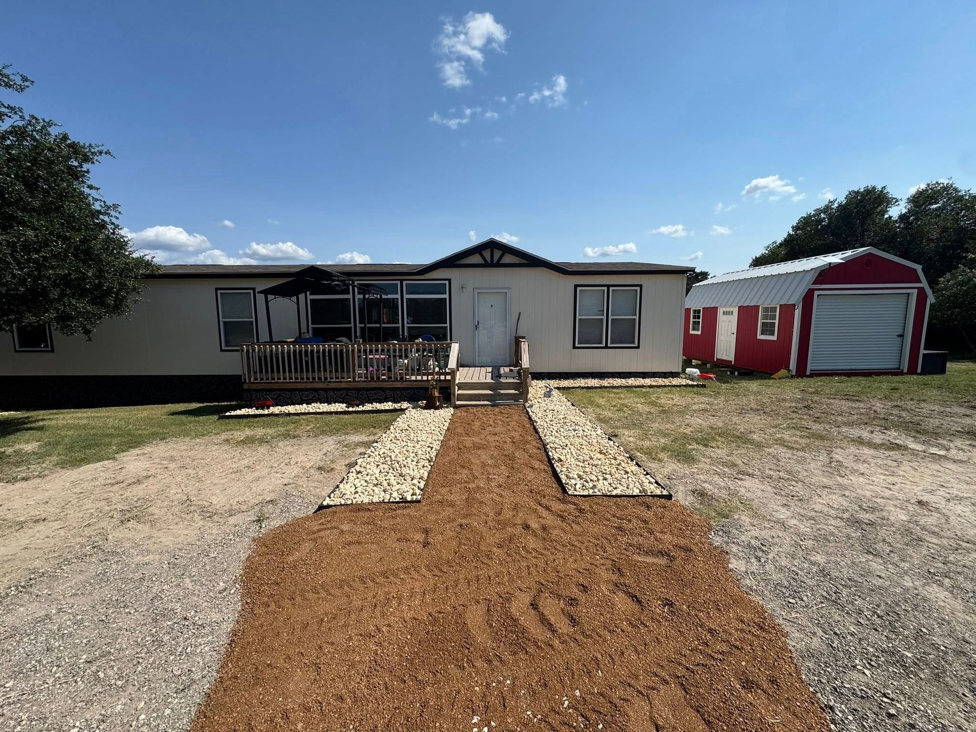 A tan mobile home with a small deck and a red garage sits under a blue sky.