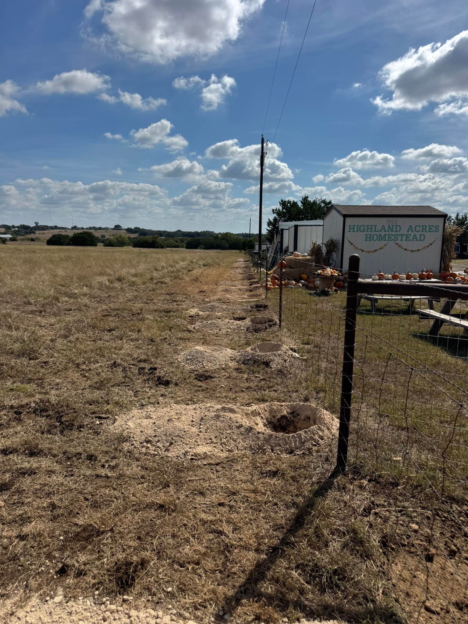A field with a fence bordering a building under a partly cloudy sky.