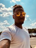 A man wearing sunglasses and a white shirt is taking a selfie