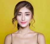 A woman wearing a necklace and earrings is standing in front of a yellow background.