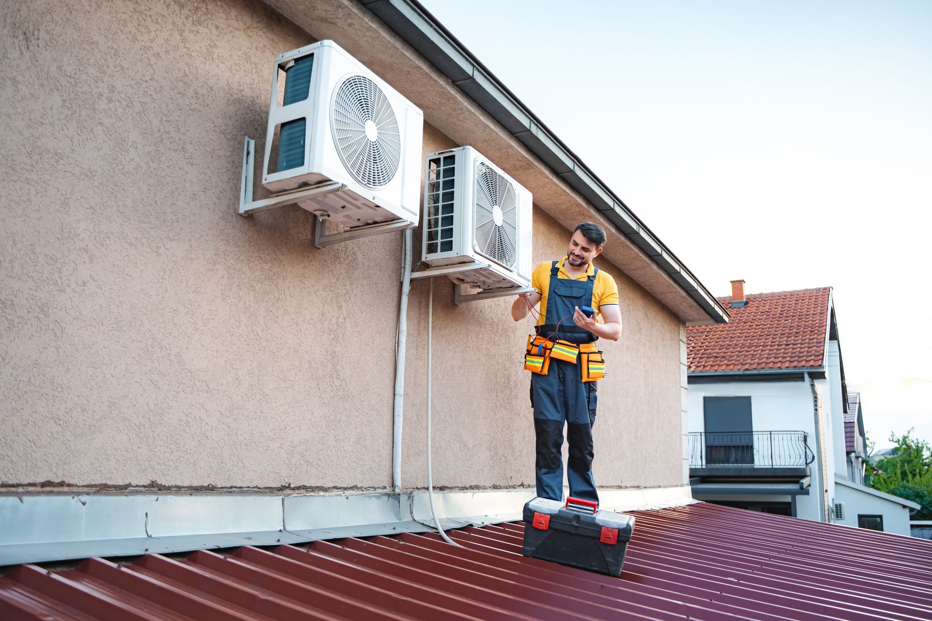 A technician using a smartphone is installing two air conditioning units on a roof.