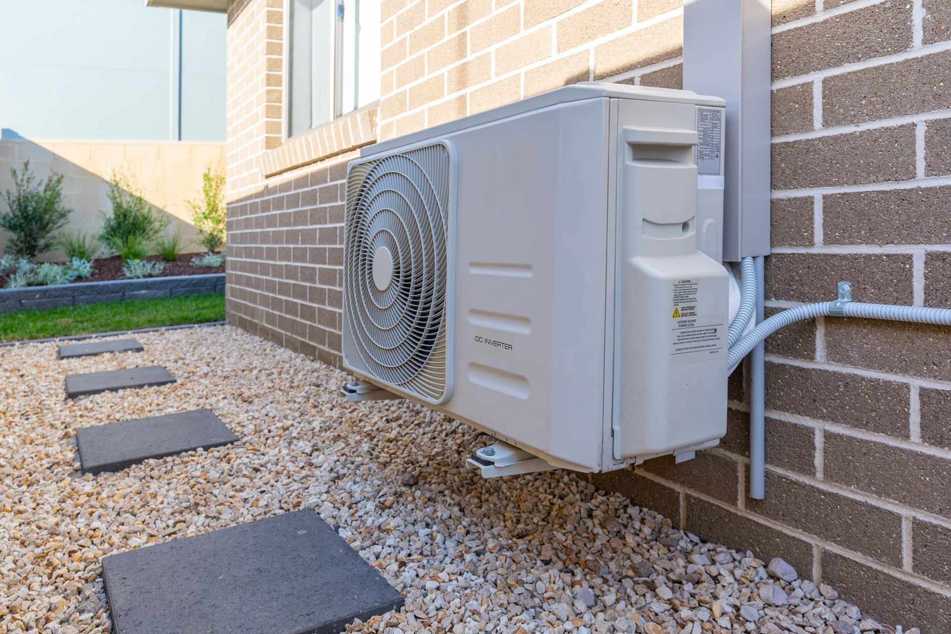 Close view of an air conditioning unit outside a house with a gravel path below it.