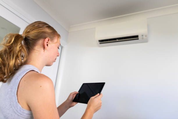A young woman controlling an air conditioner with a tablet computer.