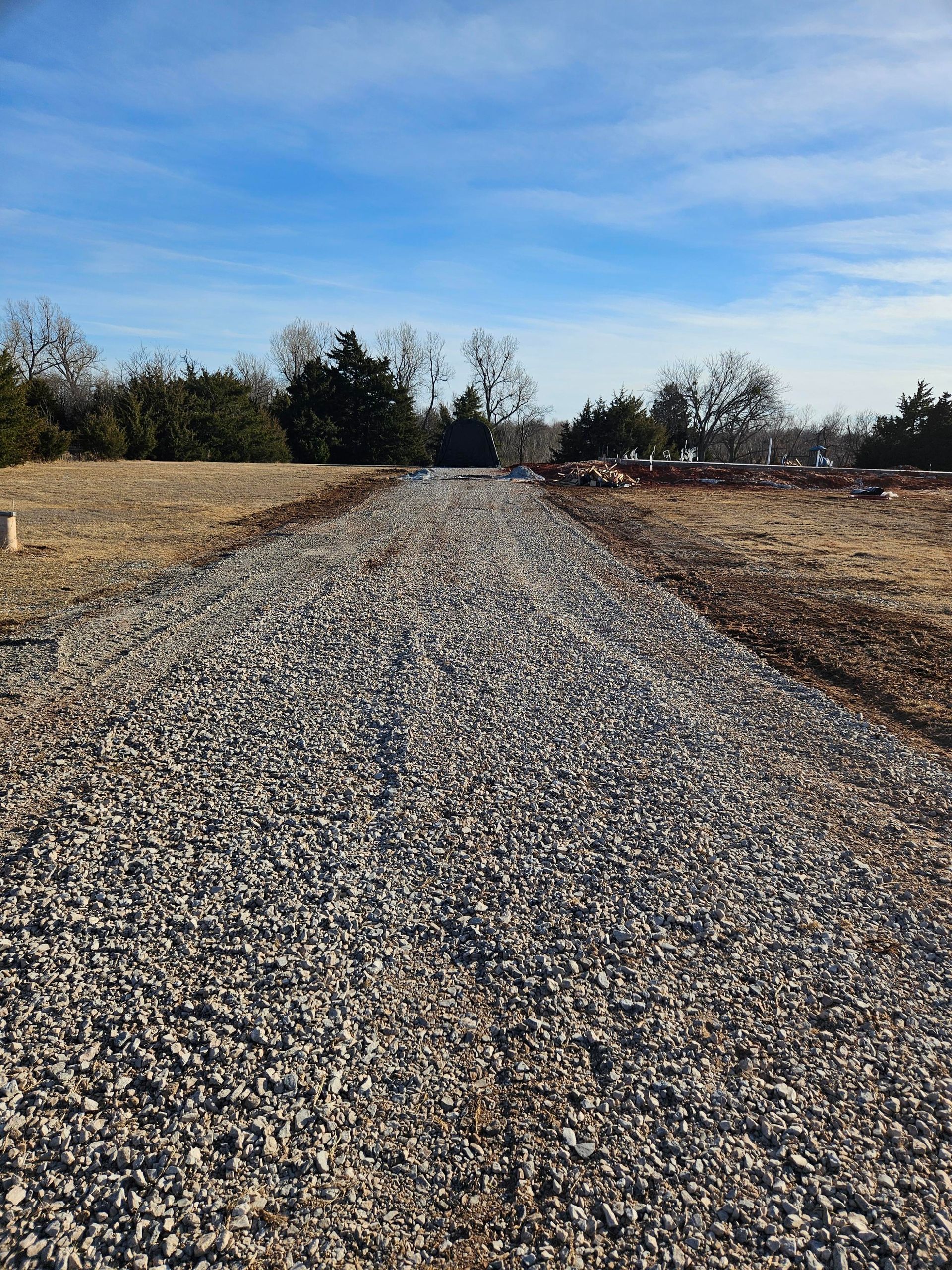 Silver semi-truck loaded with rectangular wooden pallets on a rural road under a blue sky.