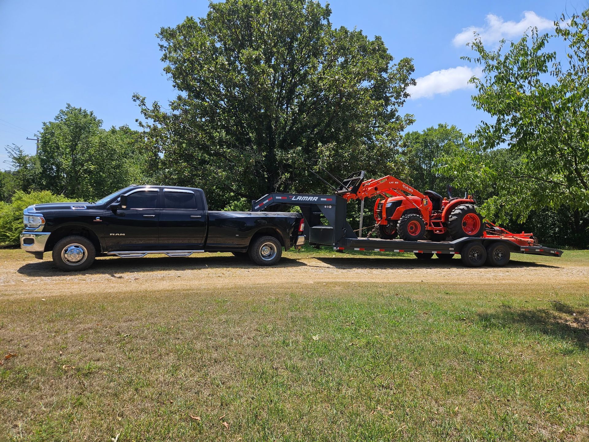 Red tractor with disc harrow, driving on gravel road next to grass.