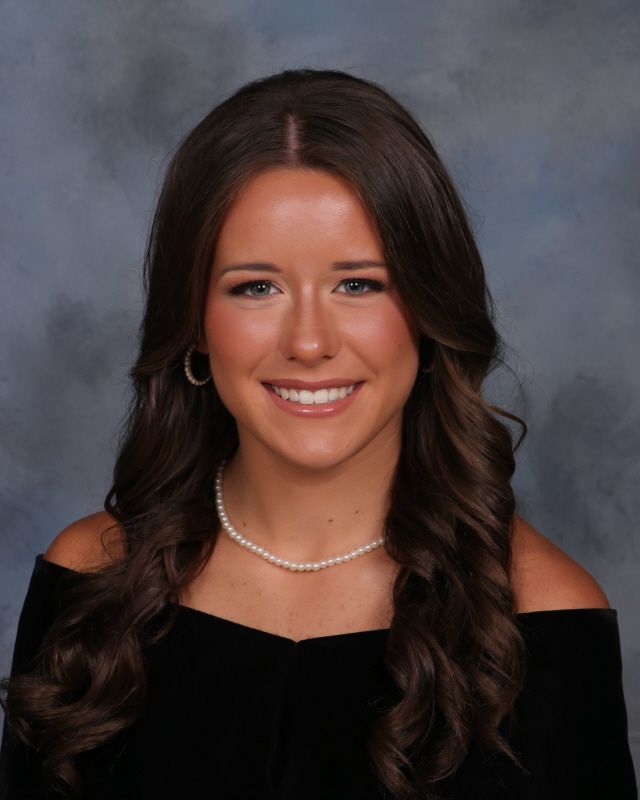 A portrait of a person with curly dark hair, wearing braces, a pearl necklace, and an off-the-shoulder black top.