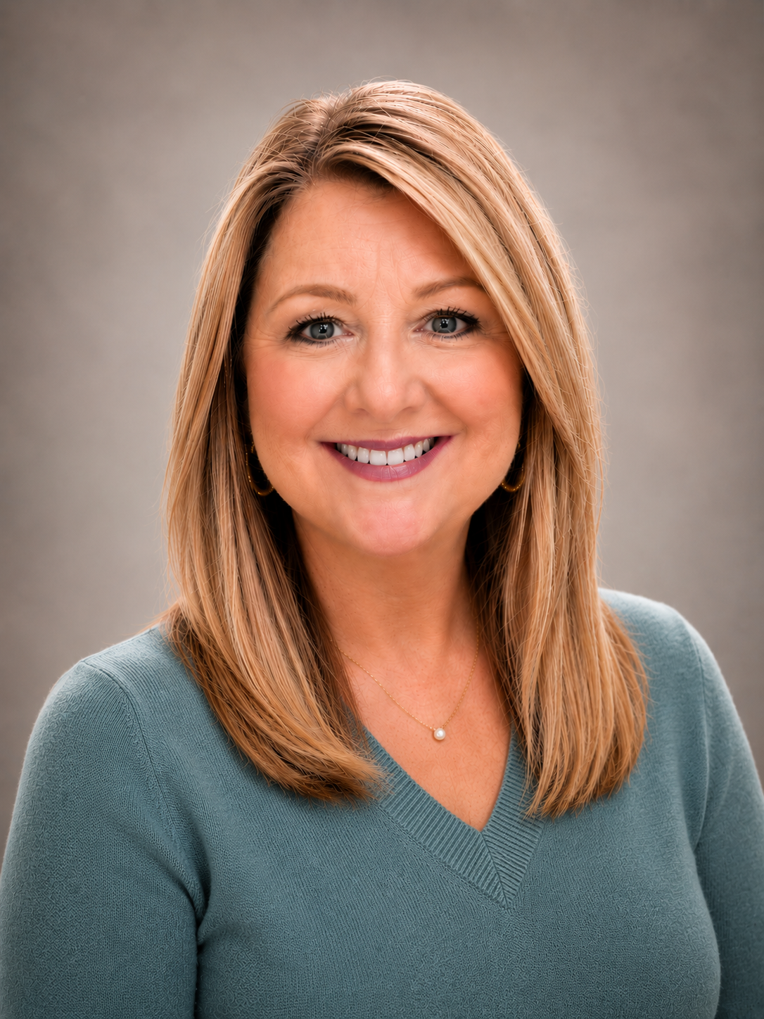 Smiling woman with shoulder-length blonde hair, wearing a dark blue blazer and burgundy top against a blue background.