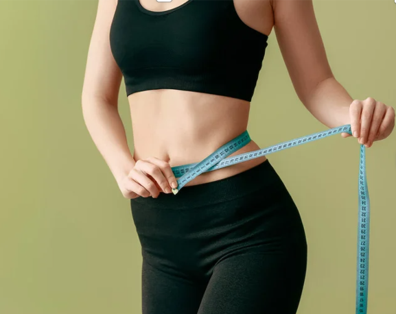 Woman in black activewear measuring her waist with a blue tape measure. Semaglutide treatment