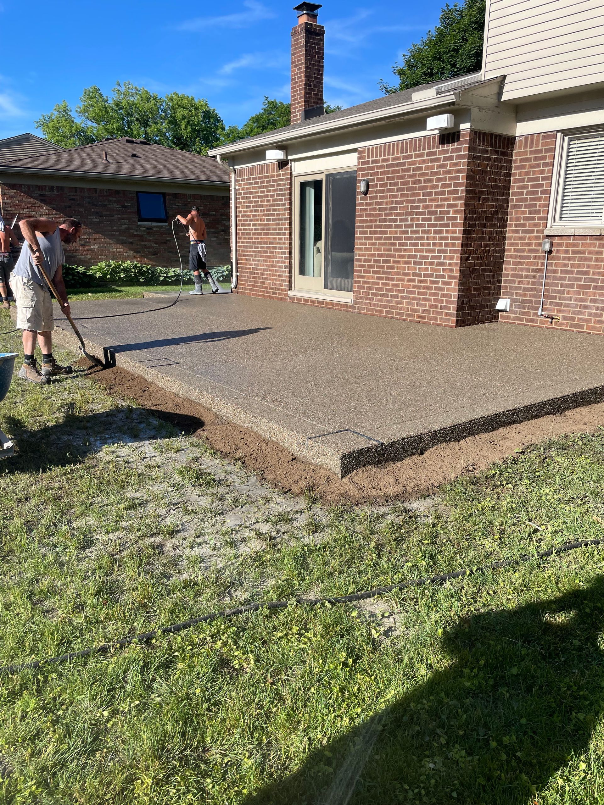 A group of people are working on a concrete patio in front of a brick house.