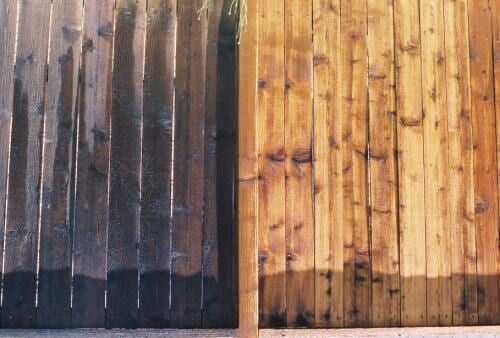 Wooden fence, half stained dark brown, half light wood.