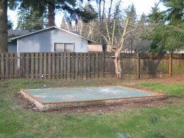 A concrete pad in a grassy backyard, with a wooden fence and shed in the background.