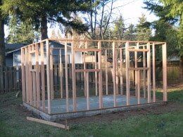 Wooden shed frame under construction on a concrete foundation in a yard.