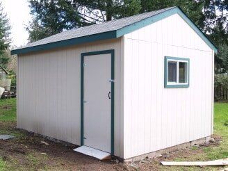 Beige shed with green trim, door, and window; set on a grassy area.