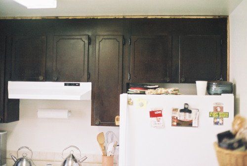Dark brown kitchen cabinets above a white refrigerator with items on top.