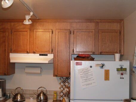 Kitchen with wooden cabinets, white refrigerator, and stovetop with kettles.