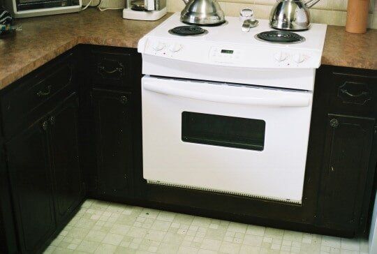 White oven and stovetop against dark brown cabinets and a tan countertop.