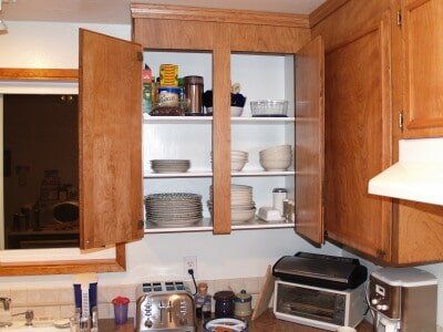 Wooden kitchen cabinets with open doors, revealing shelves of dishes and food items.