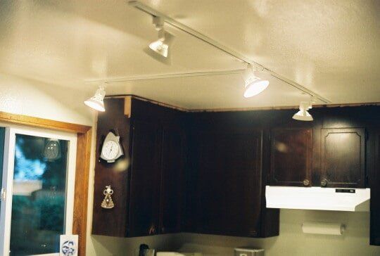 Track lighting installed on a kitchen ceiling, illuminating dark wooden cabinets and a window.