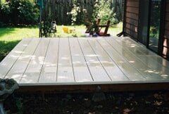 Wooden deck in a backyard, slightly elevated, with bright, light-colored planks.