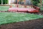 A red wooden train track in a yard with a deck.
