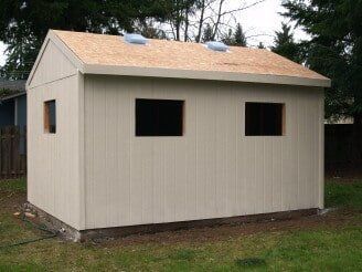 Tan storage shed with three windows, a light brown roof, and two vents. Set on grass.