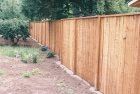 Wooden privacy fence in a yard with grass and trees.
