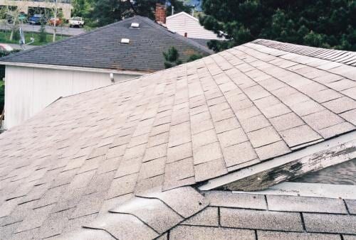 Shingled roofs on houses, seen from above; gray shingles, some moss.