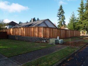 Wooden fence surrounding a house with a retaining wall and sidewalk.
