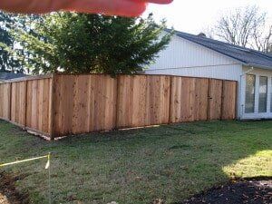 Wooden privacy fence surrounding a grassy yard next to a white house with windows.