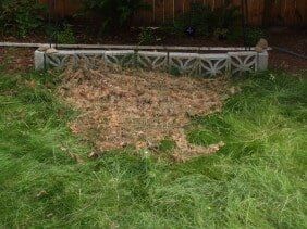 Pile of brown mulch on green grass near a decorative concrete wall.