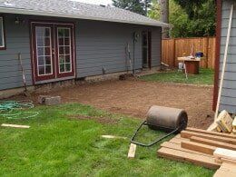 Backyard with French doors, cleared area of dirt, lawn roller, lumber, and a wooden fence.
