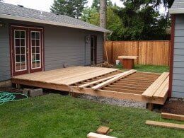 Wooden deck under construction next to a house with a door.