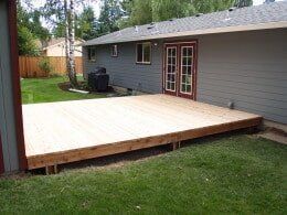 Wooden deck attached to a gray house, with grass yard and a French door.