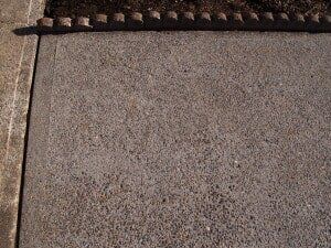 Concrete sidewalk with a row of brown brick bordering a patch of soil.