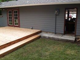 Wooden deck, steps, and concrete path leading to a door on the side of a house with gray siding.
