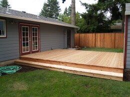 Wooden deck with steps leading to a house with red-framed French doors and a green lawn.
