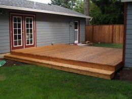 Wooden deck with two steps attached to a gray house.