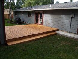 Wooden deck with two steps leading to double doors on a gray house.