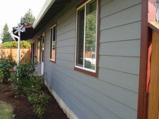 Gray house with brown trim and windows, surrounded by landscaping.