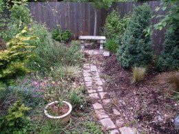 Brick pathway through a garden with a wooden fence. 