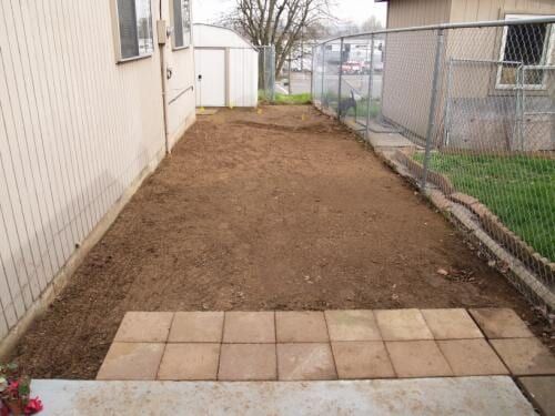 A small backyard with bare dirt, a paved area, and a fence.
