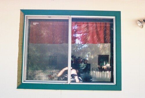 Window with green frame reflecting trees and interior with red curtain.
